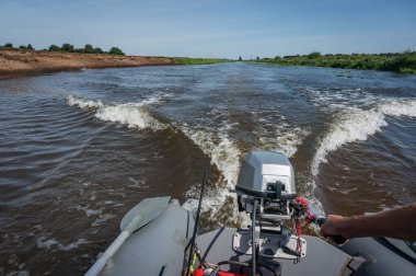 Bir motorlu tekne dar bir nehirde iz bırakır ve dalgalar saçar.