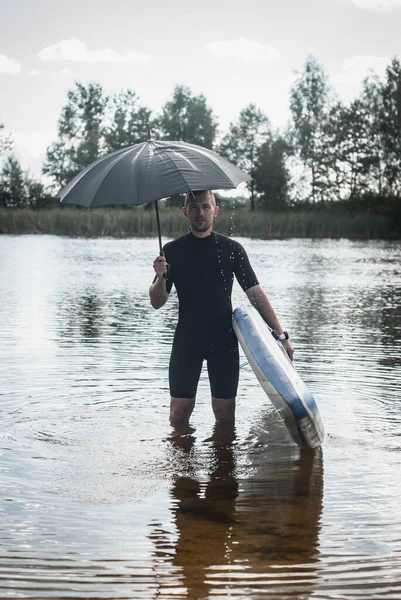 Un surfista con un paraguas se para en el agua, el concepto de mal tiempo — Foto de Stock