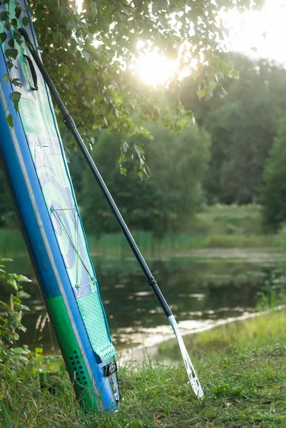 Nafukovací prkno a pádlo na pozadí jezera v letní den — Stock fotografie
