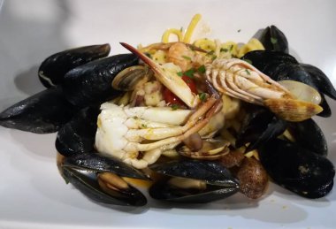 Beyaz seramik tabakta midyeli, midyeli, balıklı ve maydanozlu makarna.