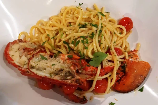 Beyaz seramik tabakta ıstakoz, maydanoz ve kiraz domatesli spagetti