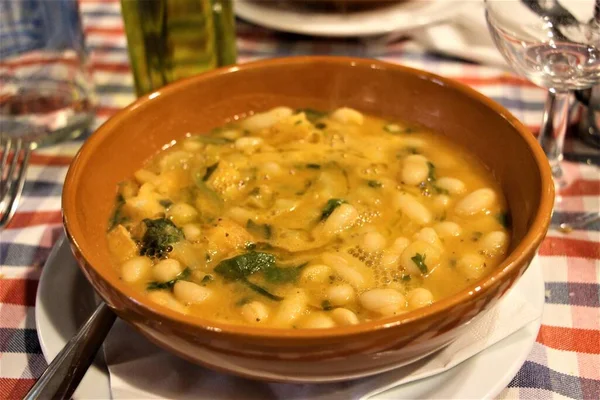 Mavi beyaz ve kırmızı kareli masa örtüsü olan tipik bir İtalyan restoranı masasında terakotta yağlı fasulye çorbası.