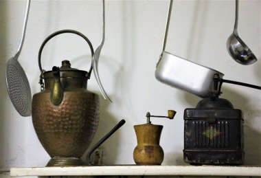 İtalyan mutfağının eski eşyaları, kepçeler, kahve öğütücüleri ve sürahiler beyaz rafta.