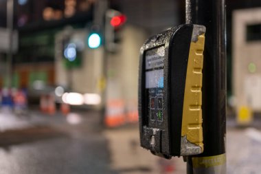 Pedestrian crossing button in Glasgow Scotland 2021 with night city lights and blurry background.