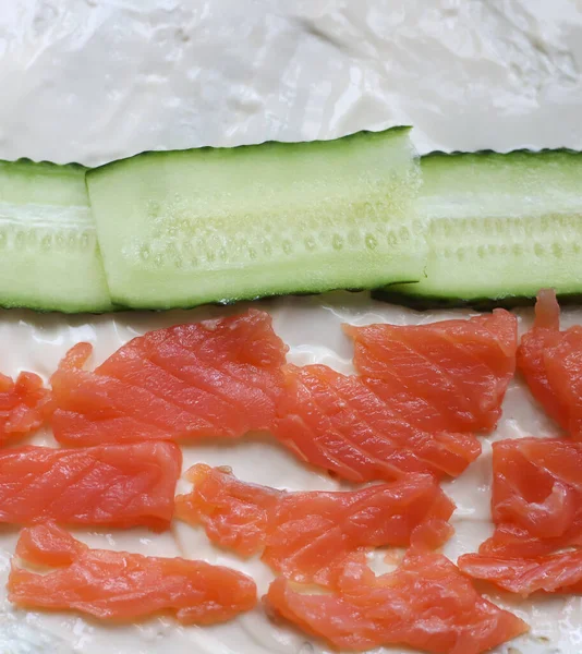 red fish salmon cut into pieces next to a green juicy cucumber cut into slices lies on pita bread spread with melted cheese close-up. for store flyers banners