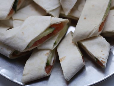 Dilimlenmiş pita rulosu eritilmiş peynirle doldurulmuş kırmızı tuzlu somon ve bahçeden gelen sulu yeşil salatalık beyaz arka planda bir tabakta. Not defterlerinin el ilanları için.