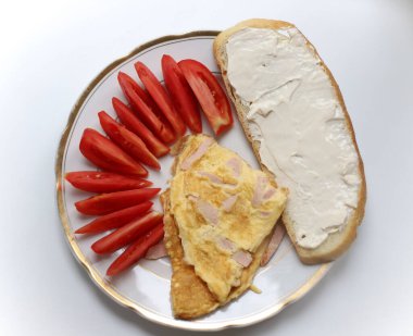 Bahçıvandan erimiş peynir ve kırmızı domates dilimleri içeren bir sandviçin yanında altın kenarlı beyaz bir tabakta sosisli omlet. Yemek kitaplarının ve not defterlerinin reklam afişleri için.