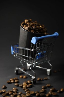 Mavi saplı metal bir alışveriş arabasında siyah bir kahve çekirdeği ile dolu siyah bir el arabası var. Kahve dükkanlarının sokak menüleri için el ilanları.