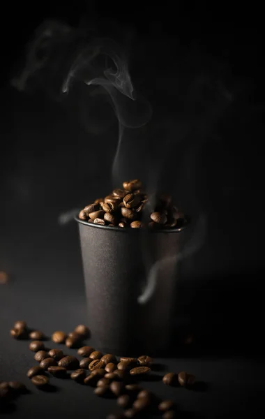 黒を背景に コーヒー豆と茶色と白の煙とガラスの周りに散在する穀物でいっぱいの黒いクラフトグラスが近くにあります コーヒーハウス ストリートメニュー カフェ ラベル チラシ バナー — ストック写真