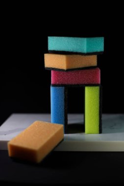 Tabakları yıkamak için mutfak süngerleri ve farklı renkte sarı mavi turuncu ve pembe yüzeyler koyu arkaplan üzerinde gri çizgiler bulunan beyaz mermer bir tahtada uzanıyor.