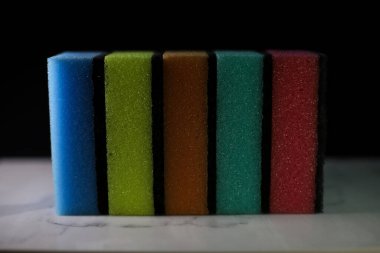 Tabakları yıkamak için mutfak süngerleri ve farklı renkte sarı mavi turuncu ve pembe yüzeyler koyu arkaplan üzerinde gri çizgiler bulunan beyaz mermer bir tahtada uzanıyor.