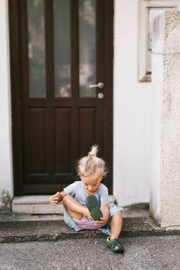 Little girl sits on the steps of the house and pours water out of her sandals. High quality photo