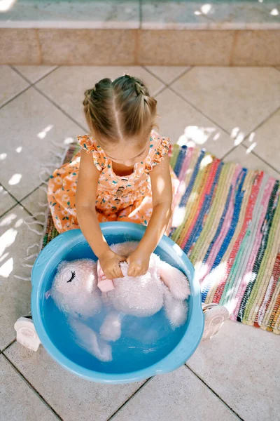Little girl diligently lathers and rubs a soft toy in a bowl. High quality photo