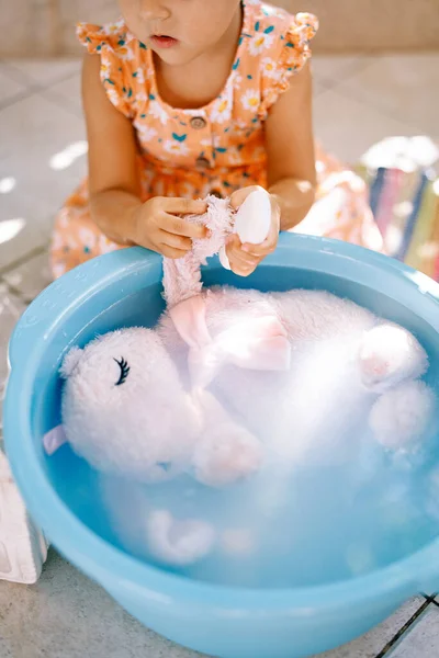 Little girl washing a soft toy in a bowl. High quality photo