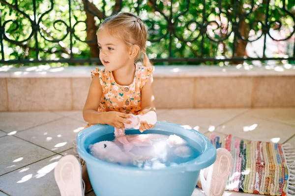 Little girl washes a soft toy on the balcony. High quality photo