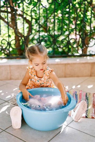 Little girl washes a soft toy in a bowl on the balcony. High quality photo