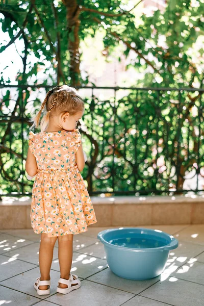 Little girl stands on the balcony near a large bowl of water. High quality photo
