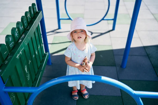 Little girl in a panama hat stands on the playground and looks up. High quality photo