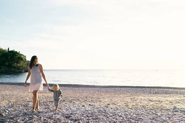 Mom and little girl are walking along the seashore holding hands. High quality photo