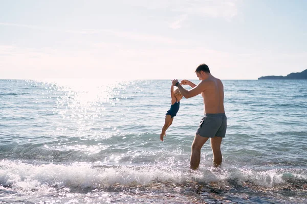 Dad raises the hands of a little girl above the water in the sea. High quality photo