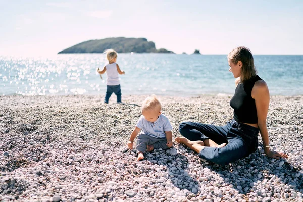 Little boy sorting through pebbles while sitting with his mother on a pebble beach. High quality photo
