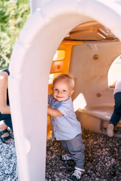 Little boy hides peeking out in a toy house on the playground. High quality photo