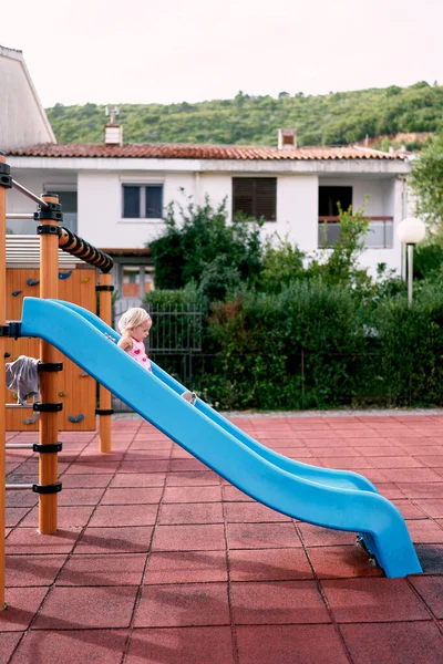 Little girl slides down a slide on a playground. Side view. High quality photo