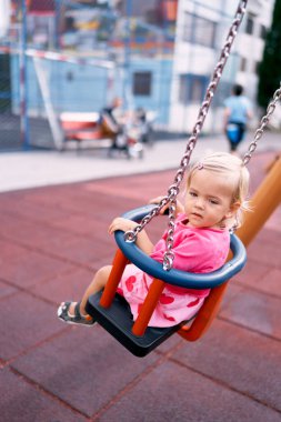 Little girl swings on a chain swing and looks thoughtfully to the side. High quality photo