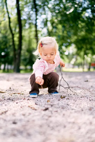 Little girl draws on the ground with a stick. High quality photo