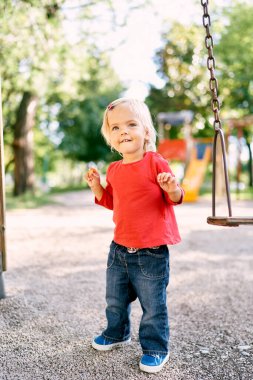 Little girl stands on the playground smiling slyly. High quality photo