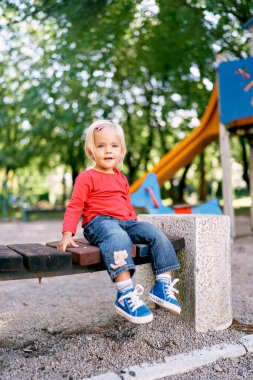 Smiling little girl sitting on a wooden bench in the park. High quality photo