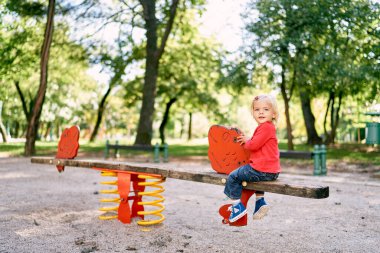 Little girl sits turned back on a wooden balance beam in the playground. High quality photo