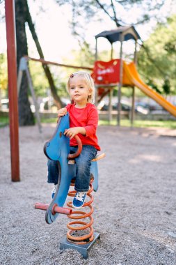 Little girl sits on a spring swing-balancer in the park. High quality photo