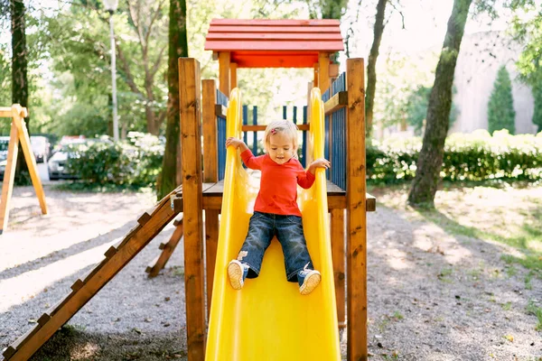 Little girl slides down a bright slide at the playground in the park. High quality photo