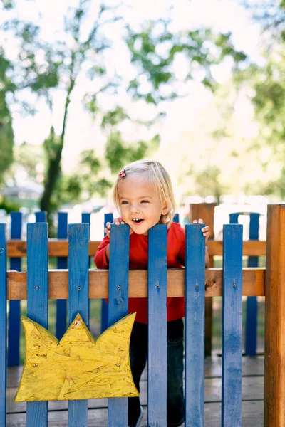 Little smiling girl leans on a wooden fence in the playground. High quality photo