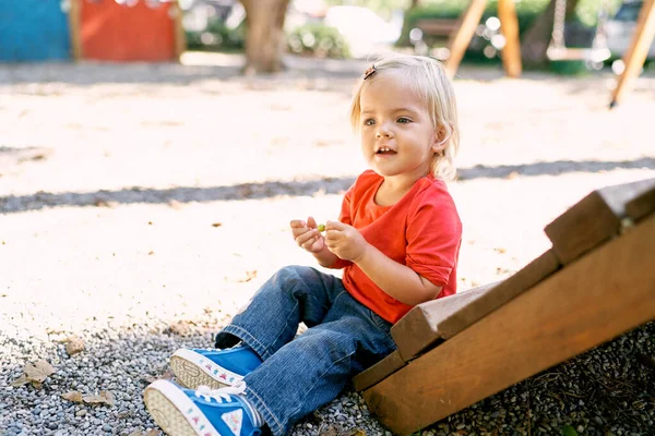 Little girl sits on the gravel near the wooden stairs on the playground. High quality photo