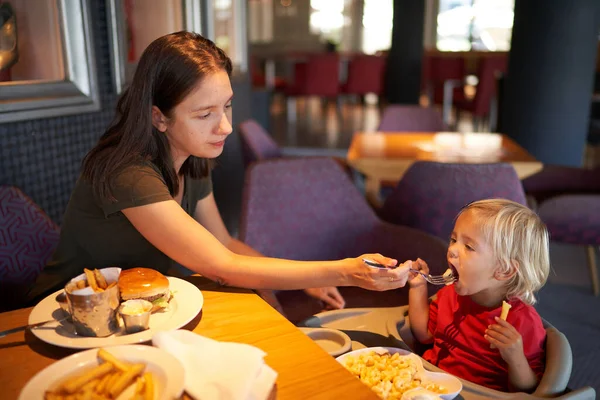 Mom feeds a little girl sitting on a highchair in a restaurant. High quality photo