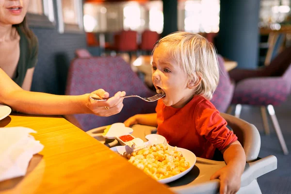 Mom feeds a little girl with a fork in a restaurant. High quality photo