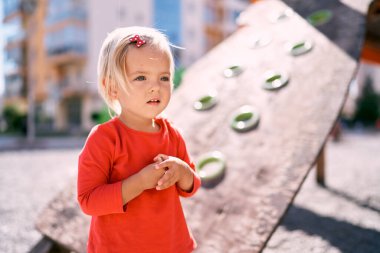 Little girl stands near the climbing wall on the playground. Portrait. High quality photo