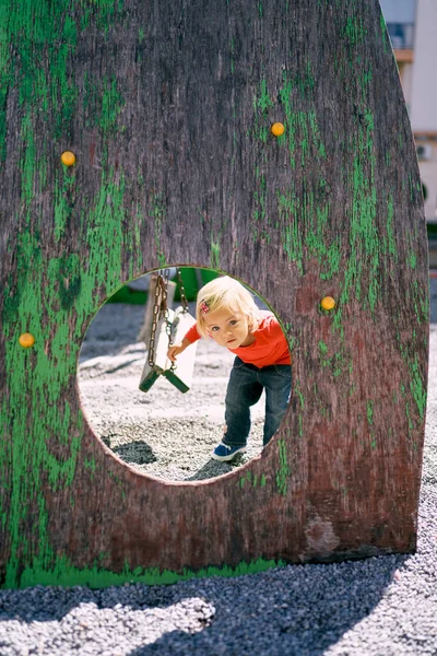 Little girl on the playground peeking through a round hole in the wall. High quality photo