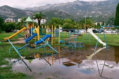 Huge puddle in front of a playground on a green meadow in front of houses. High quality photo