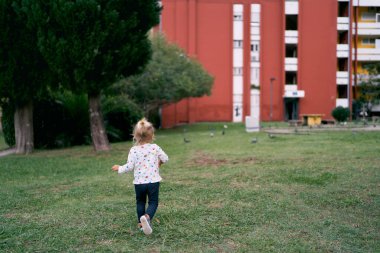 Little girl runs across the green lawn towards an apartment building. High quality photo