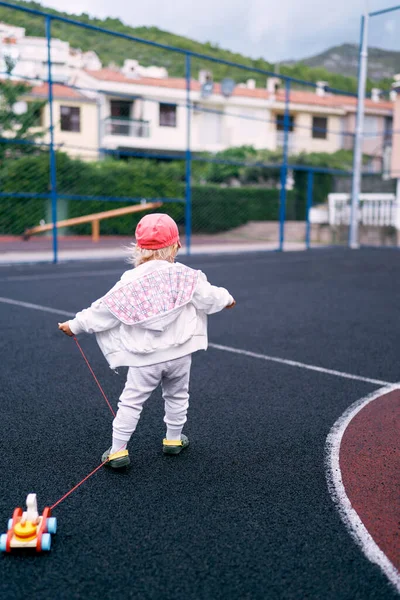 Little girl walks on the sports ground with a toy car. High quality photo