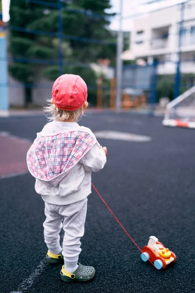 Little girl is standing on the sports ground with a toy car. Back view. High quality photo