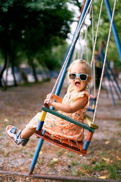 Little girl swings with her head turned and her mouth open on a swing. High quality photo