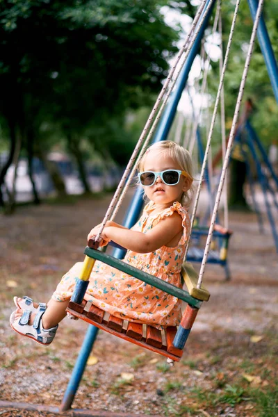 Little girl swings with her head turned on a swing. High quality photo