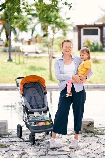 Åldrad Kvinna Står Med Liten Flicka Famnen Nära Barnvagnen Högkvalitativt — Stockfoto