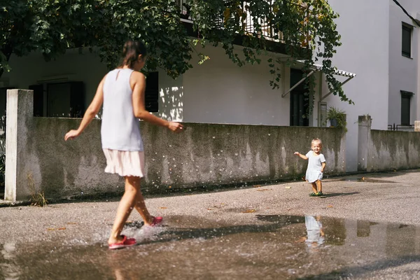 Mom stands in a puddle and splashes water on a little girl. High quality photo