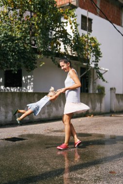 Annem su birikintisinde dururken elini tutan küçük bir kızı döndürür. Yüksek kalite fotoğraf