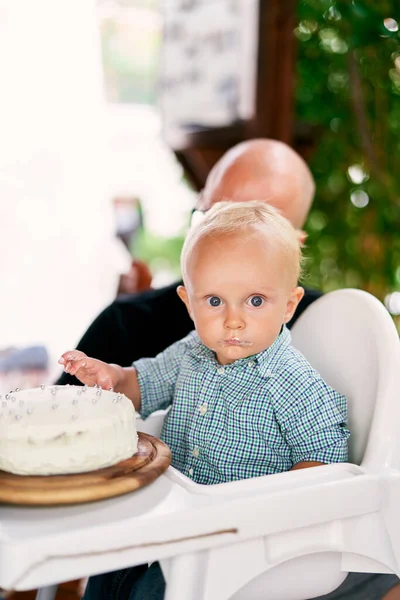 Küçük çocuk sandalyeye otururken parmaklarıyla pastadaki kremayı deniyor. Yüksek kalite fotoğraf